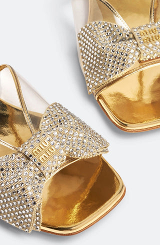 Planet Luxury Brands imzalı, kristal işlemeli fiyonk detaylı, altın rengi metalik düz taban Miu Miu sandalet