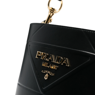 Planet Luxury Brands imzalı, altın tonlu metal logolu ve geometrik dikiş detaylı siyah deri Prada kova çanta