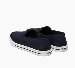 Planet Luxury Brands imzalı, lacivert Re-Nylon kumaştan üretilmiş, topuk kısmında Prada logolu erkek slip-on ayakkabı.