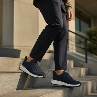Planet Luxury Brands lacivert Prada spor ayakkabı, merdivenlerde yürüyen bir modelin ayağında, modern ve şık tasarım.