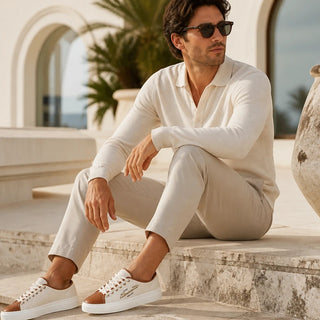 Planet Luxury Brands Santoni Caelum bej kanvas ve deri sneaker giyen şık bir erkek, dış mekan ortamında oturuyor.